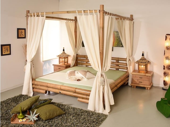 Lit à baldaquin en bambou avec rideaux blancs dans une chambre tropicale entourée de végétation